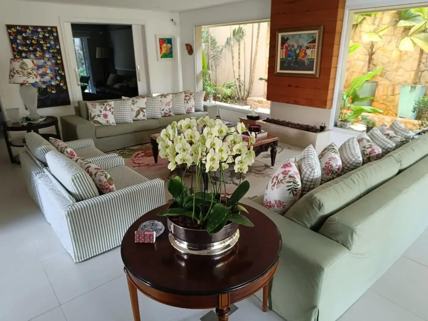 Sala com sofás claros, obras de arte e jardim