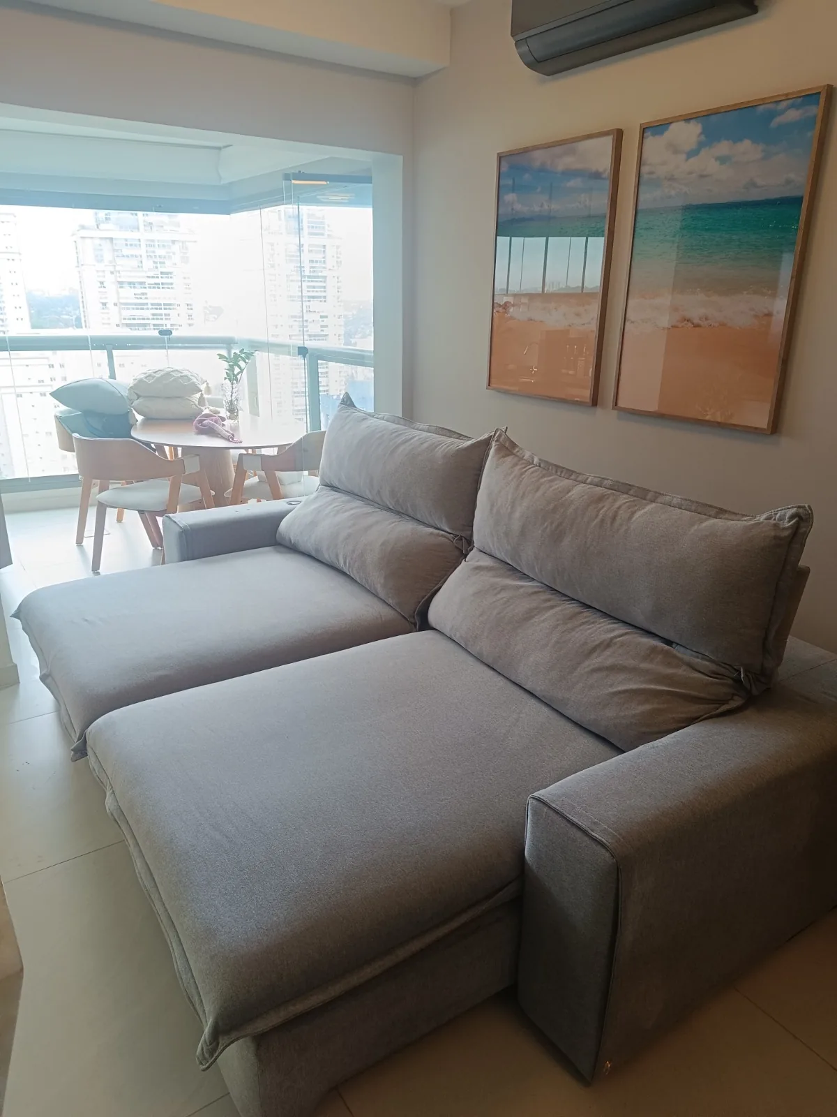 Sofá cinza retrátil em sala com varanda e quadros