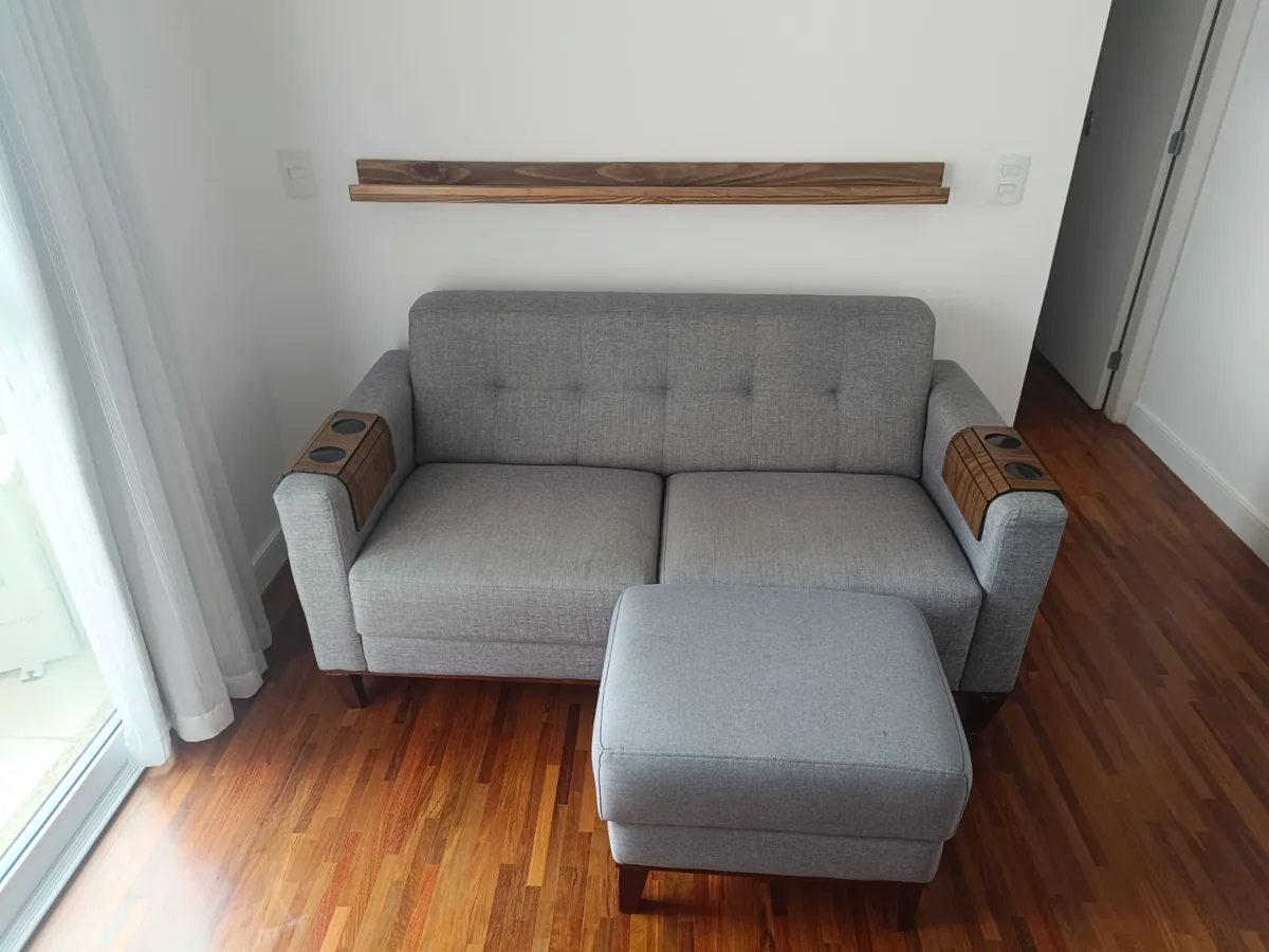 Sofá cinza de 2 lugares com puff sobre piso de madeira